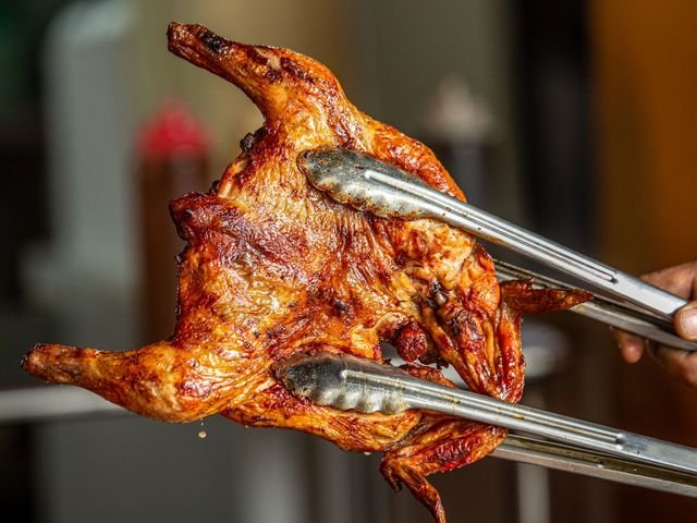 Ayam bakar madu utuh dijepit penjepit di atas panggangan