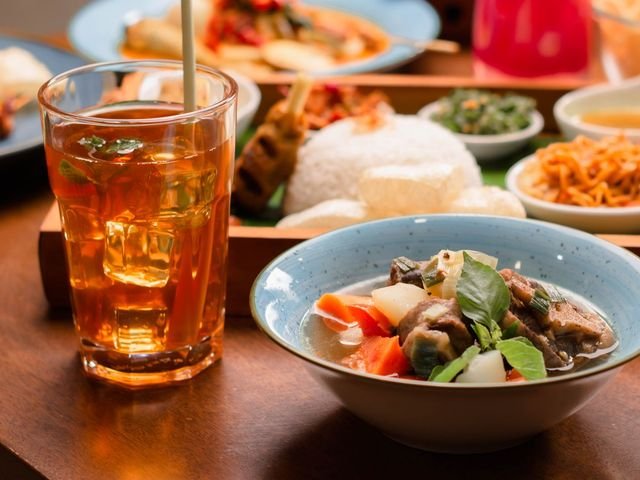 Es teh manis di gelas tinggi di samping semangkuk sayur