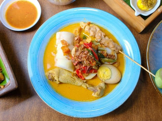Lontong sayur di piring biru dengan telur dan sambal