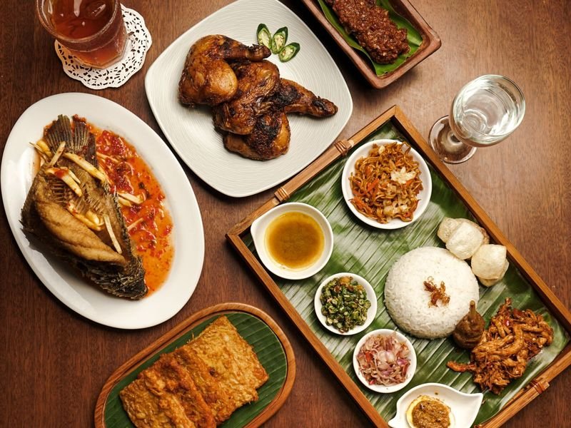 Nasi box lengkap dengan ayam bakar, sate, dan lalapan di atas daun pisang
